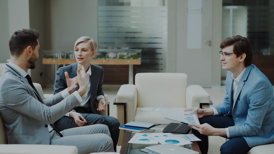 Home businessman discussing financial reports with female and male business partners sitting on sofa in modern office hall with indoors
